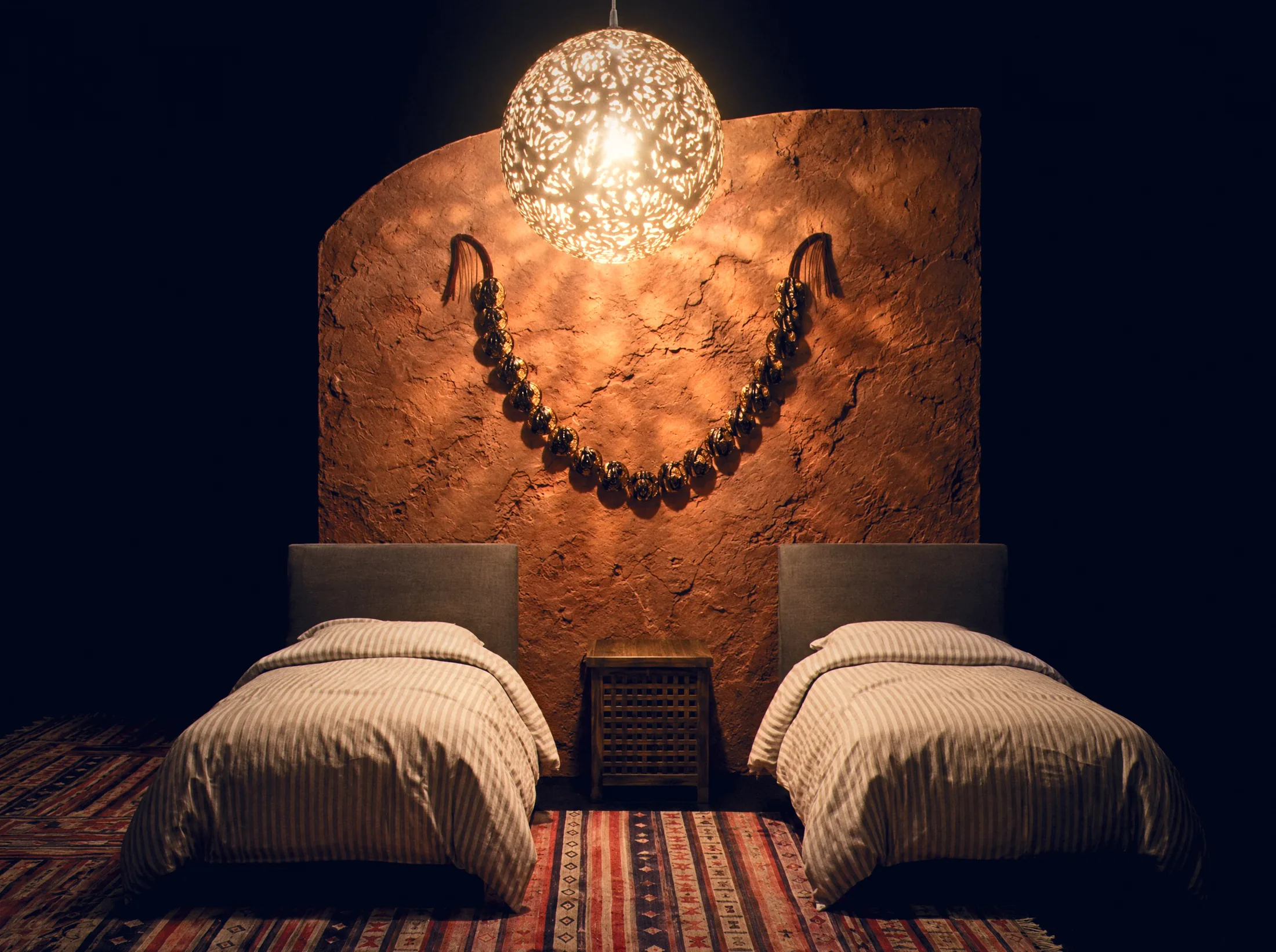 Twin beds before a clay wall under a pierced brass pendant
